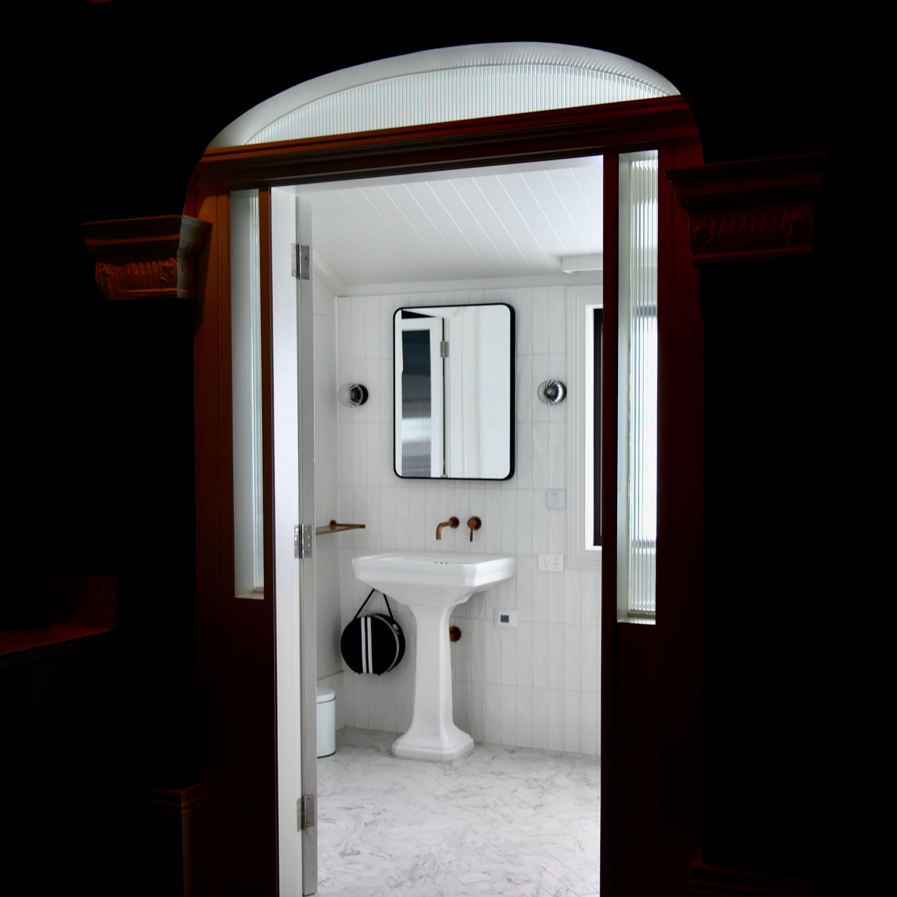 Simple pedestal basin and mirror in a bright, sparsely furnished bathroom