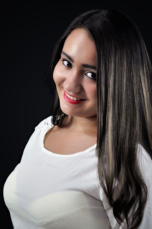 Free Portrait of a young woman smiling, showcasing long hair and casual white attire. Stock Photo