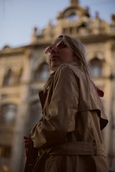 Stylish woman in trench coat and sunglasses, city backdrop.