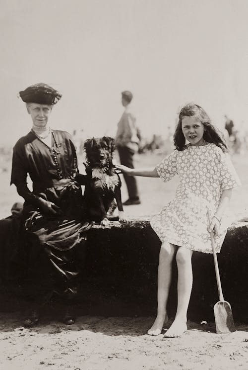 Grayscale Photo of A Girl Sitting On Concrete Bench With Her Grandmother And Dog