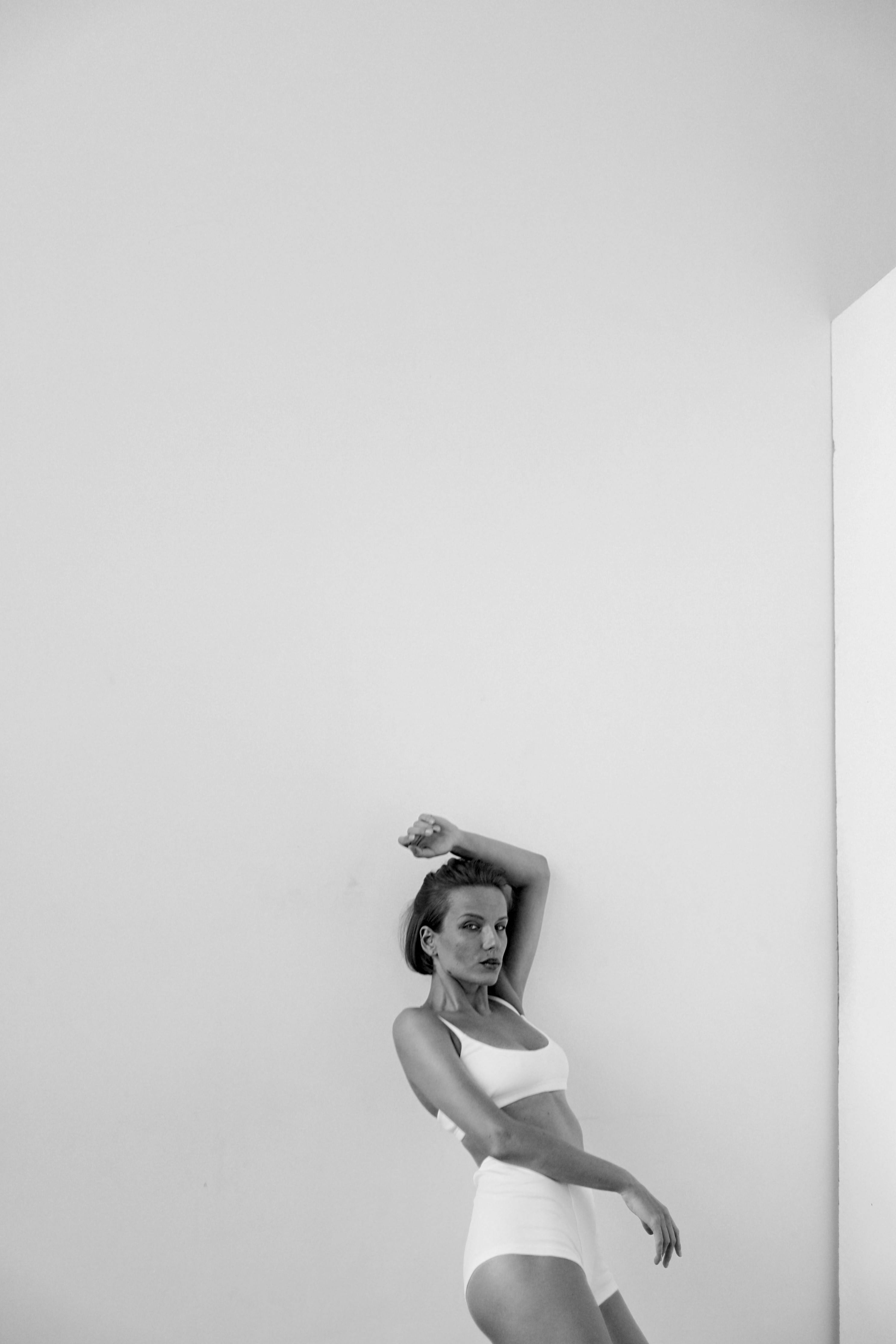 A grayscale portrait of a stylish woman posing against a minimalist indoor backdrop.