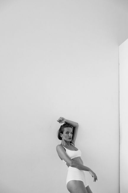 A grayscale portrait of a stylish woman posing against a minimalist indoor backdrop.