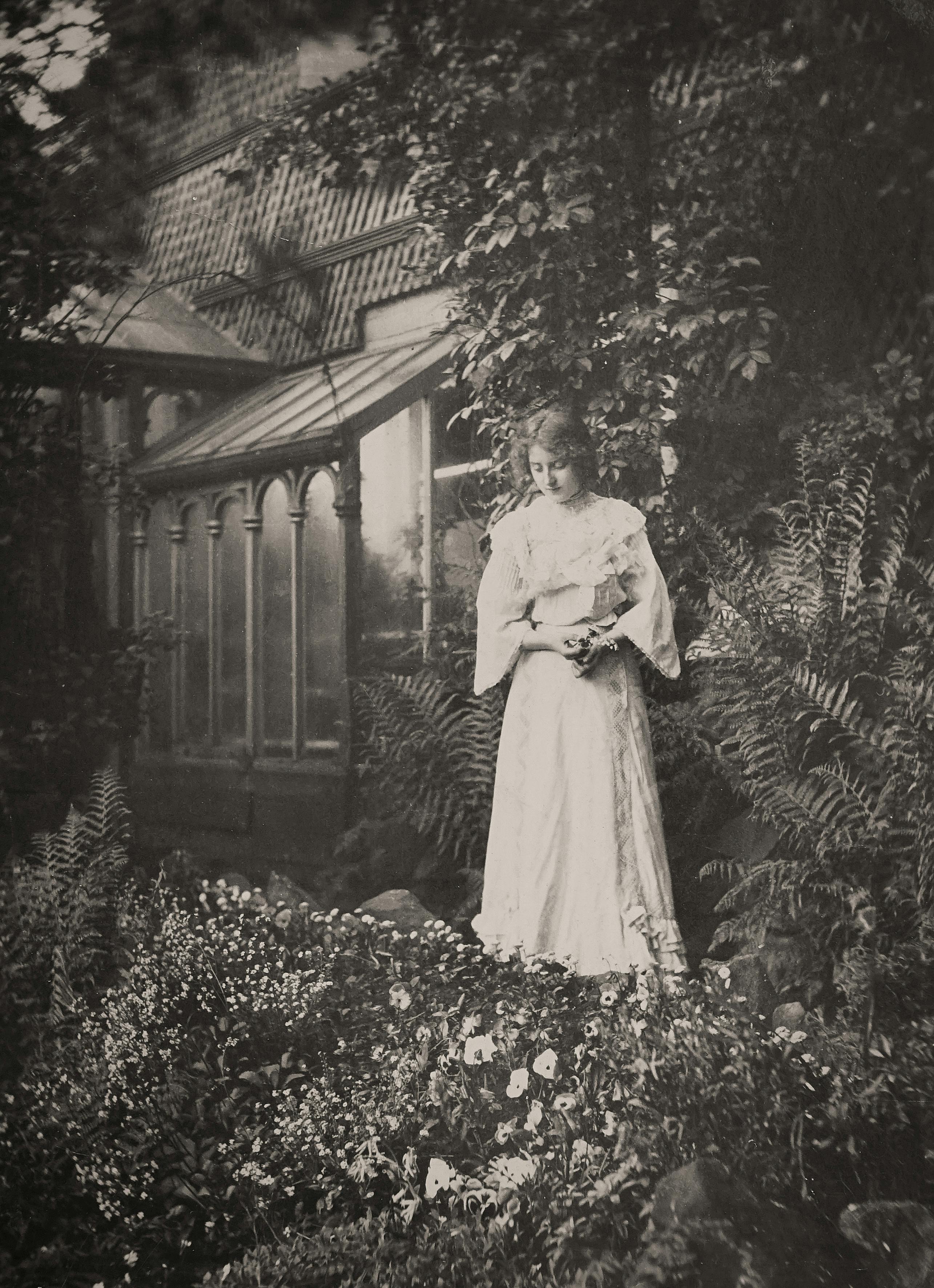 A vintage style photo of a woman in a garden surrounded by lush foliage and flowers.