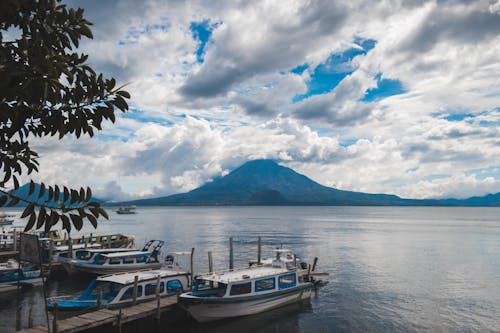 Free Docked Boats on Lake Surrounded by Mountains and Volcanoes Under Cloudy Sky Stock Photo