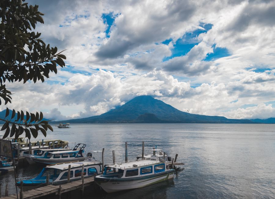 Boats docked with a stunning view of Lake Atitlan and its volcano under a cloudy sky.