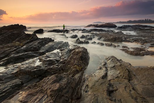 日出时分，宁静的海岸上，岩石与远处的人影共同营造出静谧的氛围