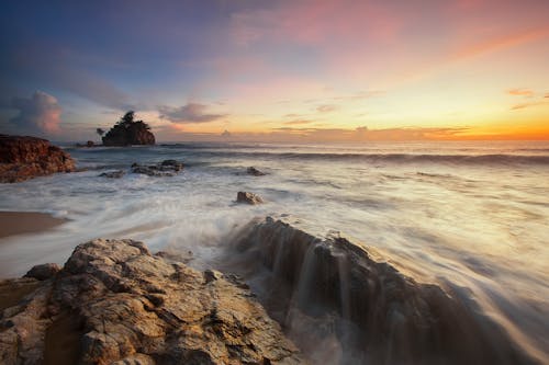 бесплатная Коричневые и серые скалы у моря во время восхода солнца Стоковое фото