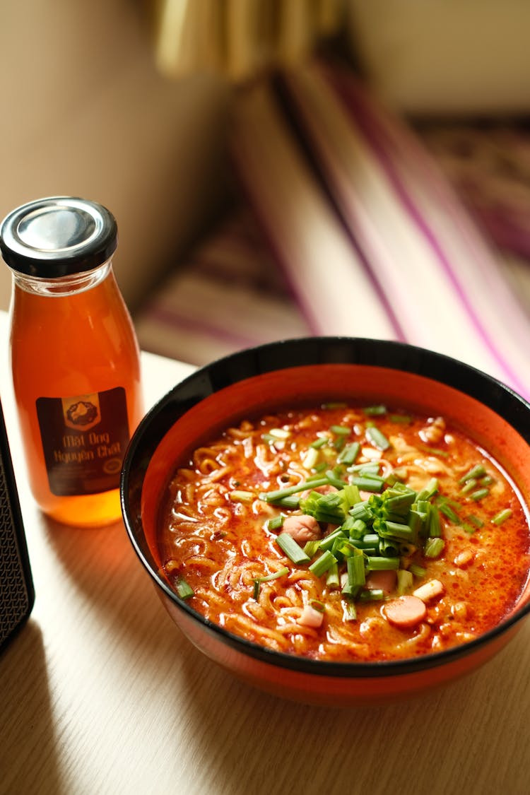 A Bowl Of Noodle Soup With A Bottle Of Juice Drink