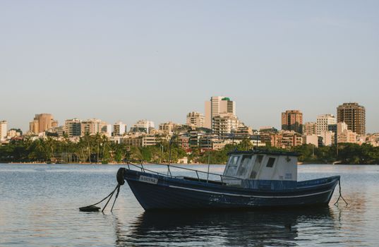 A peaceful scene of a docked boat with a city skyline at sunset, reflecting calm waters.