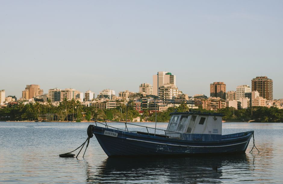A peaceful scene of a docked boat with a city skyline at sunset, reflecting calm waters.