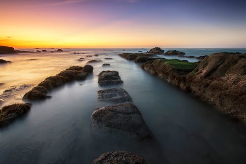 Free Tranquil ocean sunrise with smooth water and rocky shore, capturing nature's peaceful beauty. Stock Photo