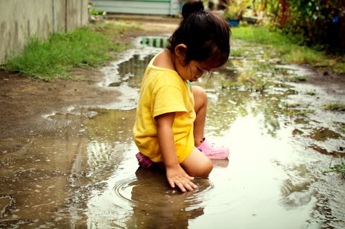 Child in Yellow Shirt Sitting on the Puddle of Water