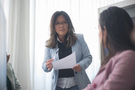 Confident Asian businesswoman in blue blazer leading an office meeting, engaging with colleagues.