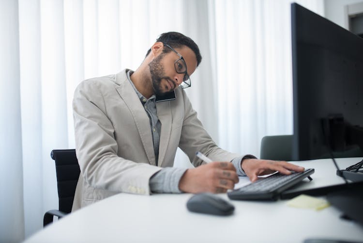 Man In Beige Suit Jacket Sitting At Table With Computer