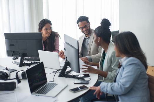 A diverse team engages in discussion around computers in a modern office setting.
