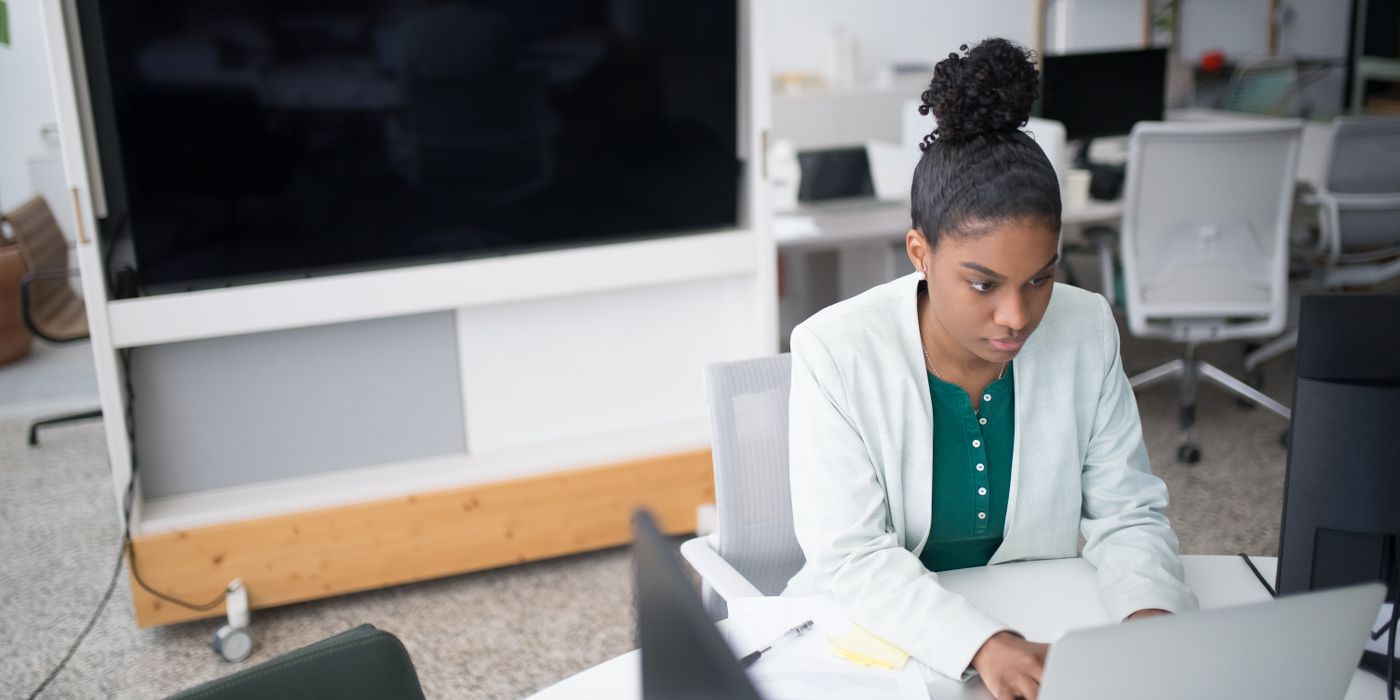 Focused woman using a laptop in a modern office setting, wearing a white blazer, working diligently.