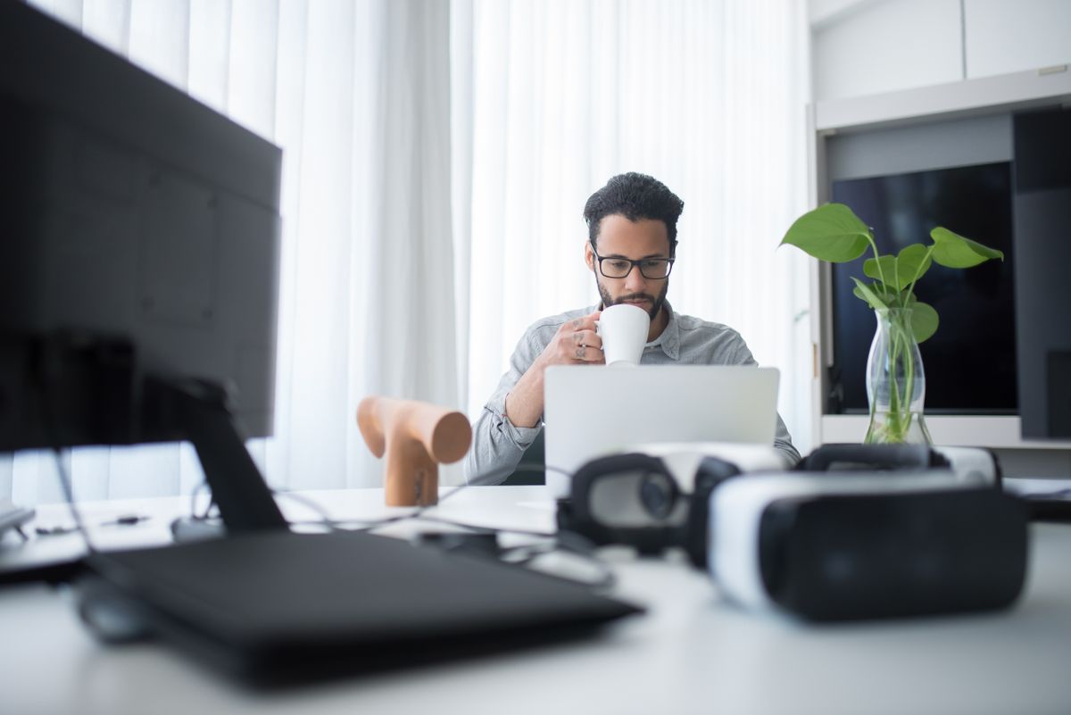 A man sipping coffee while working on a laptop at a table