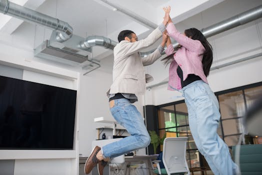 Two colleagues jumping and high-fiving in an office, symbolizing teamwork and success.