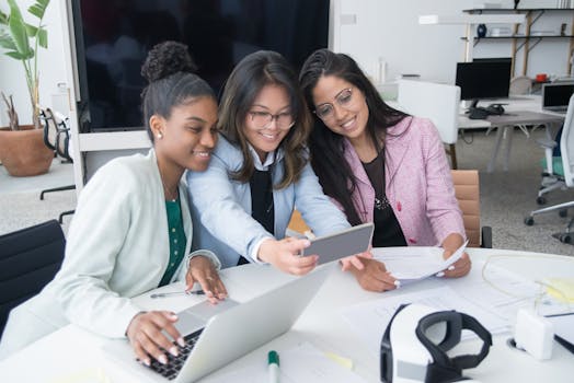 Three diverse women collaborating in a modern office, taking a selfie, showcasing teamwork and technology.