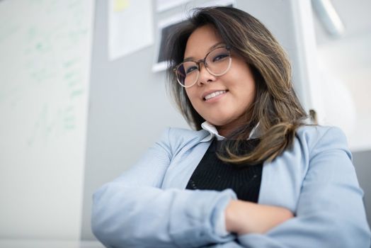 Portrait of a smiling businesswoman with glasses, confidently posed indoors with crossed arms.
