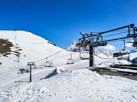 Ski lift over snowy mountains at Dombay, Russia with clear blue sky.