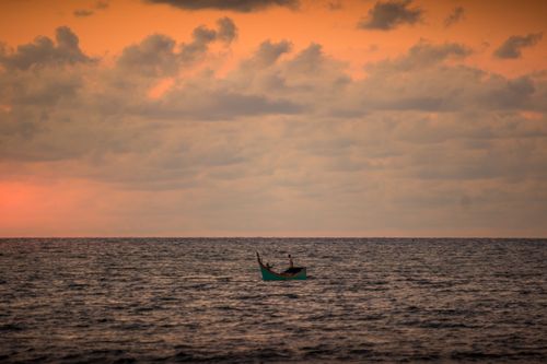 Free A lone boat floats on the calm sea under a stunning sunset sky, creating a tranquil scene. Stock Photo