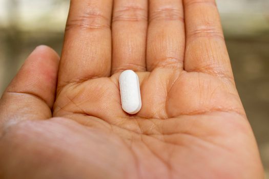 Close-up photo of a hand displaying a single white pill on the palm, symbolizing medication.