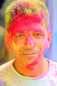 A close-up portrait of a man celebrating Holi with vibrant face colors and a joyful expression.
