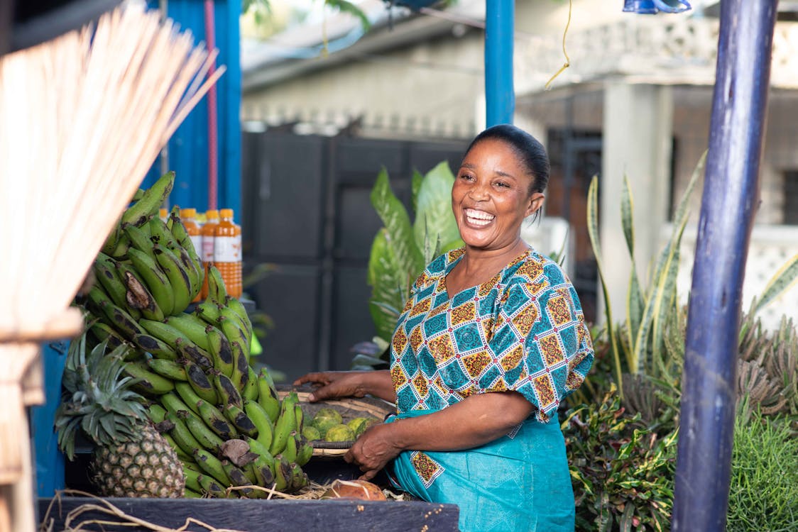 Free Woman in Blue and Yellow Floral Shirt Standing Beside the Green Banana Fruits Stock Photo