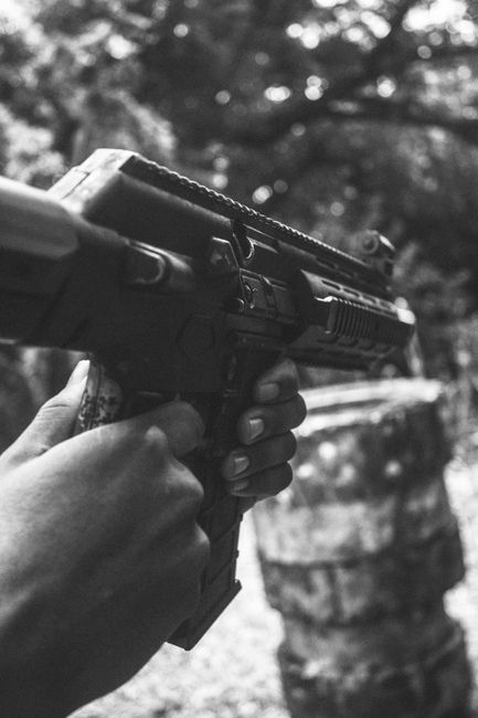 Fotomural Imagen en monocromía que muestra manos sosteniendo un arma de fuego en un entorno al aire libre, enfocada e intensa.