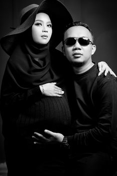 Black and white studio portrait of a stylish pregnant couple in elegant attire. - Fotografer Sidoarjo