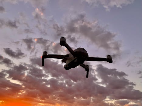 Drone flying against a colorful sunset sky, creating a stunning silhouette with clouds.