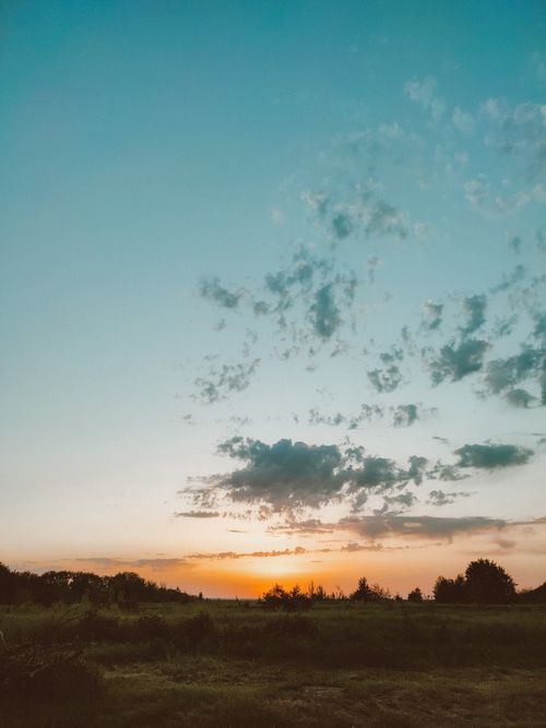 Free A tranquil sunset over a peaceful countryside field with a vibrant sky. Stock Photo