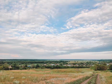 Scenic view of a serene village landscape with expansive clouds and lush greenery.
