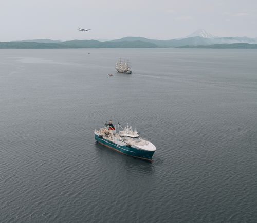 Free Drone shot capturing ships and an airplane over the vast sea with distant mountains. Stock Photo