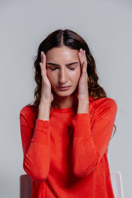 A young woman in a red sweater holding her head, depicting stress or headache.