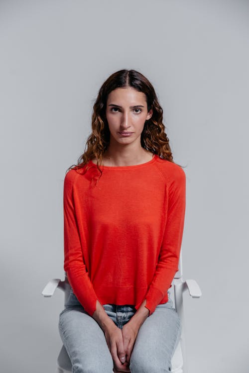 Woman in Red Long Sleeves Shirt Sitting on a Chair while Seriously Looking at the Camera
