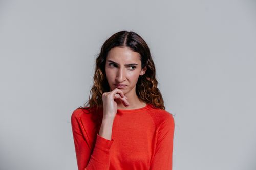 Free A woman with curly hair in a red sweater posing thoughtfully in a studio setting. Stock Photo