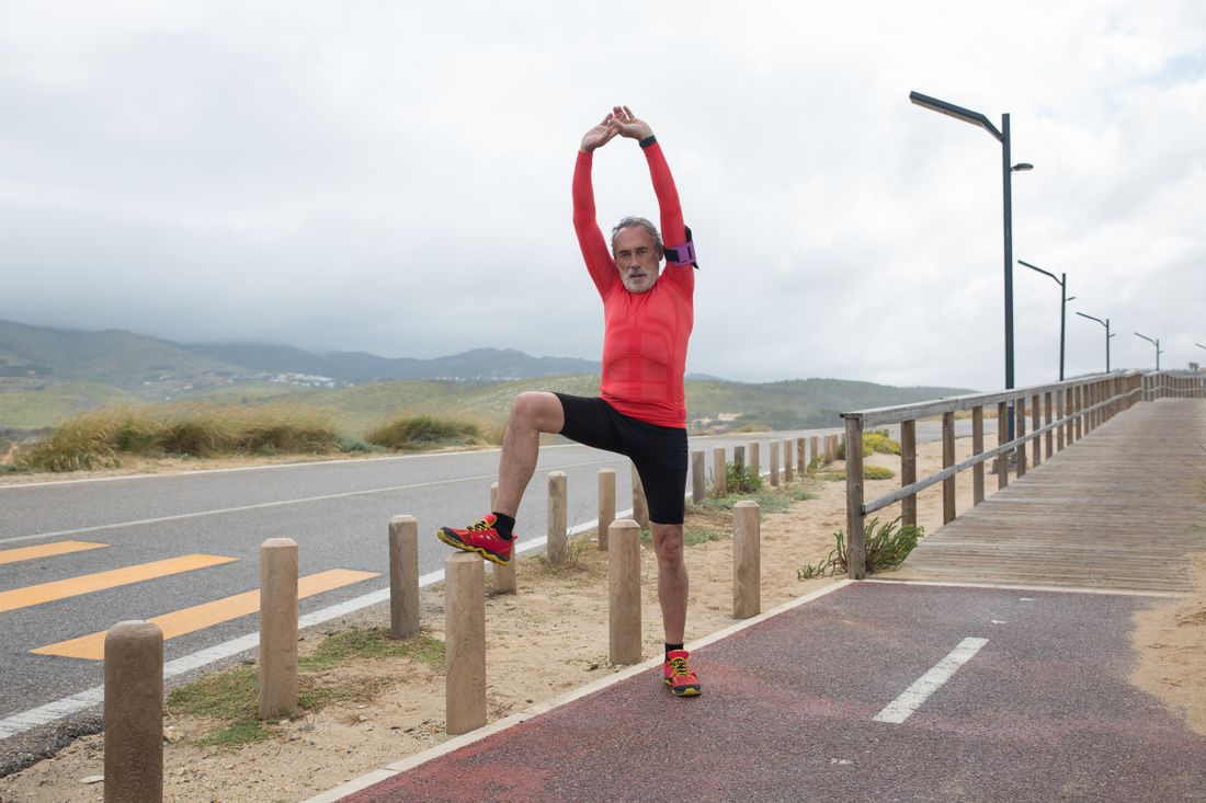 An older runner stretching beside a coastal path — photo by Kampus Production on Pexels