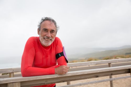 Free Elderly man in red sportswear smiling outdoors on a coastal boardwalk, Portugal. Stock Photo
