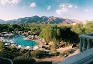 从空中俯瞰，阳光明媚的度假村游泳池被树木环绕，背景是连绵的山脉