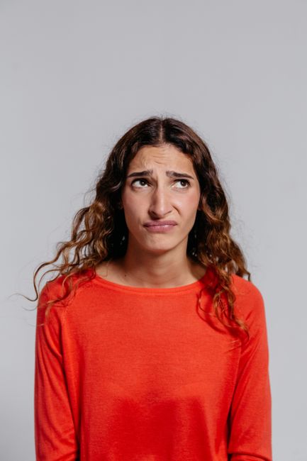 Fotomural Una mujer con un suéter naranja mostrando una expresión de descontento frente a un fondo de estudio blanco.