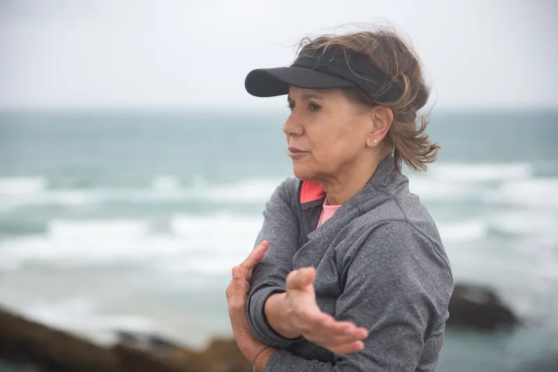 An older woman stretching her arms outdoors beside the water