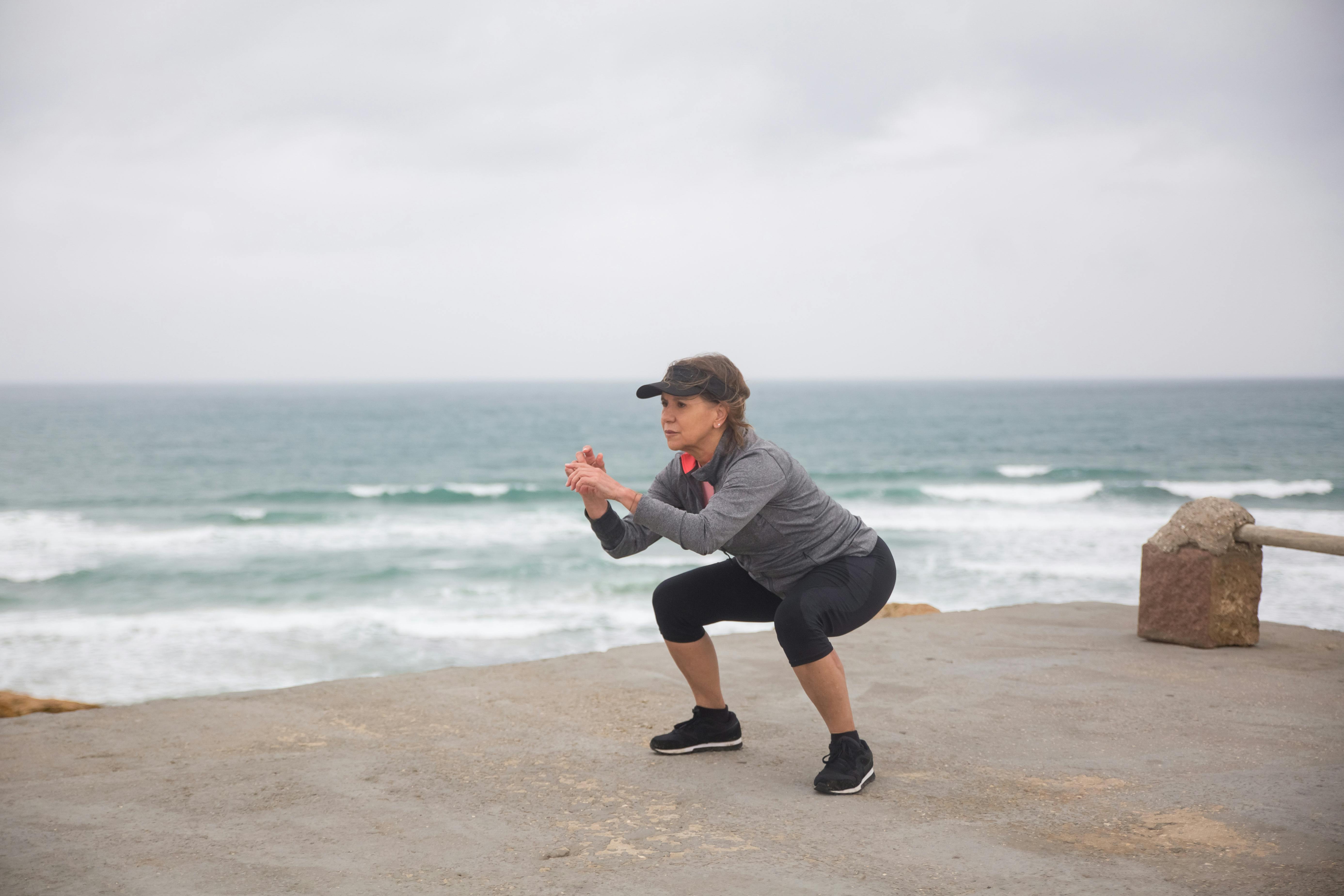 Free Woman Doing Leg Exercise Near the Ocean Stock Photo