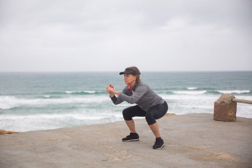 Free A senior woman performs squats outdoors by the ocean, embodying a healthy and active lifestyle. Stock Photo