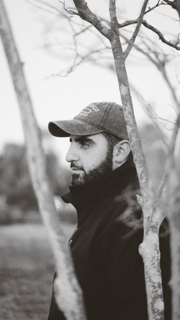Side profile of a bearded man wearing a cap captured in a park setting, black and white style.