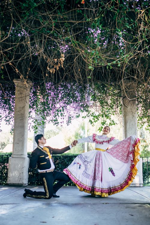 Free A couple performs a traditional Mexican dance in colorful outfits under a lush pergola. Stock Photo