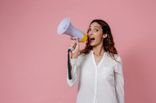 Free Woman in white shirt holding megaphone against a pink background, confidently speaking. Stock Photo