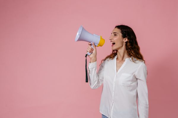 Person calling out through a megaphone on a pink backdrop — photo by Pavel Danilyuk on Pexels