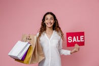 拿着购物袋和销售标志的微笑的妇女反对粉红色背景在演播室